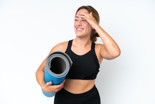 Young caucasian woman going to yoga classes while holding a mat isolated on white background smiling a lot