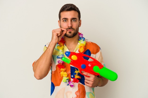 Young caucasian woman on a hawaiian party holding a water gun isolated on white background with fingers on lips keeping a secret.