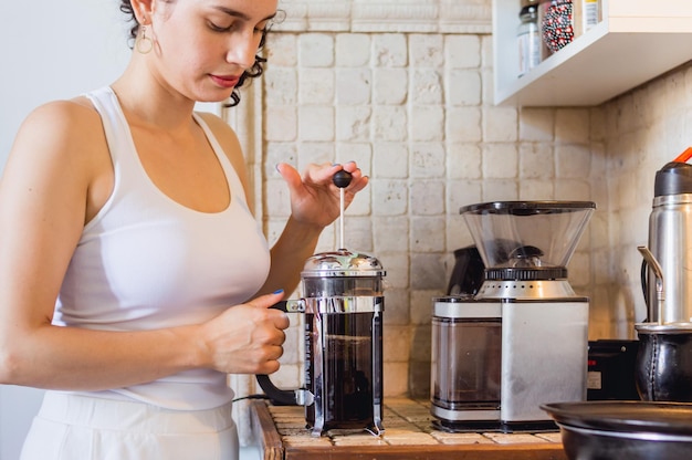 手動フレンチプレスコーヒーメーカーでコーヒーを準備している彼女の家の台所の若い白人女性