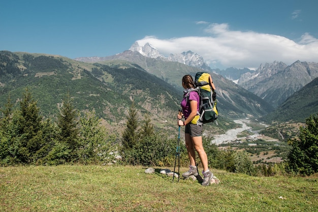 Young caucasian woman hiker from behind with backpack hiking on\
mountain trail in summer in green caucasus mountains mountain hike\
active lifestyle travel destination