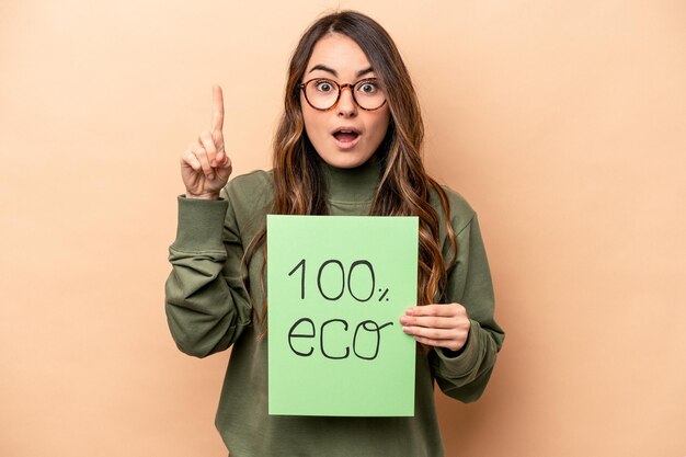 Young caucasian woman holding 100 eco placard isolated on beige background having an idea inspiration concept