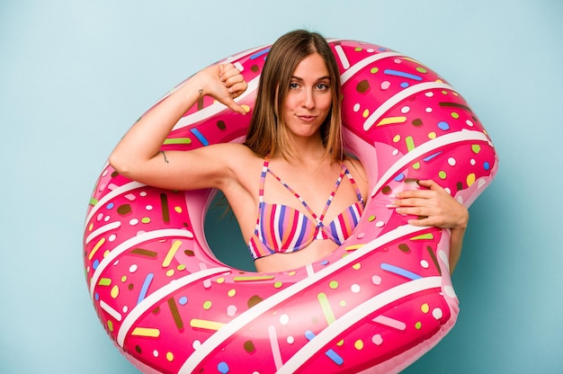 Young caucasian woman holding air mattress isolated on blue background feels proud and self confident example to follow