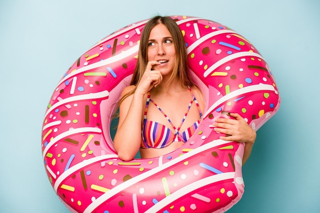 Young caucasian woman holding air mattress isolated on blue background relaxed thinking about something looking at a copy space