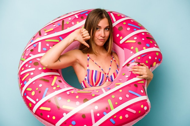 Young caucasian woman holding air mattress isolated on blue background showing a dislike gesture thumbs down Disagreement concept