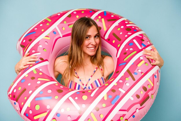 Young caucasian woman holding air mattress isolated on blue background