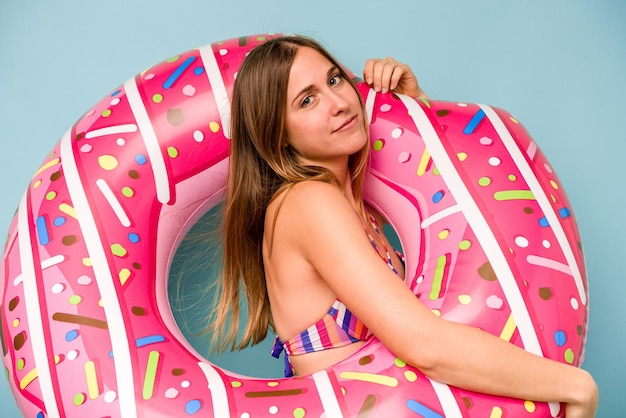 Young caucasian woman holding air mattress isolated on blue background