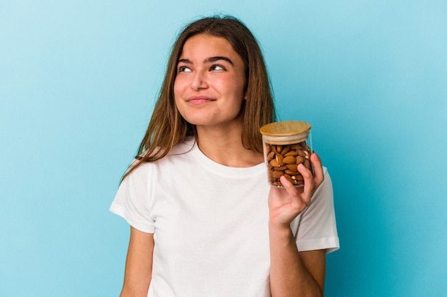 Young caucasian woman holding an almond jar isolated on blue background dreaming of achieving goals and purposes