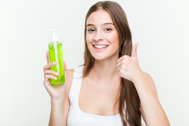 Young caucasian woman holding an aloe vera bottle smiling and raising thumb up