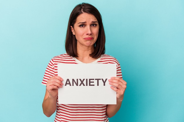 Young caucasian woman holding anxiety placard isolated on blue background