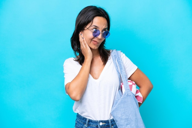 Young caucasian woman holding a beach bag isolated on blue background frustrated and covering ears