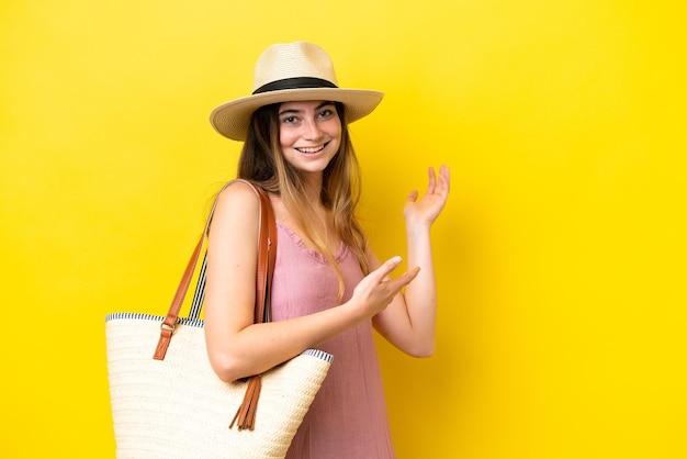 Young caucasian woman holding a beach bag isolated on yellow background extending hands to the side for inviting to come