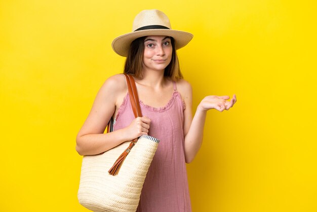 Young caucasian woman holding a beach bag isolated on yellow background having doubts while raising hands