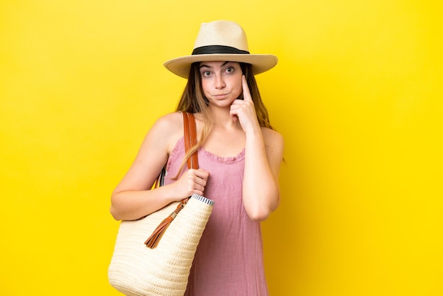 Young caucasian woman holding a beach bag isolated on yellow background thinking an idea