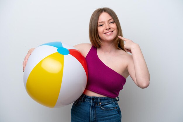 Young caucasian woman holding beach ball isolated on white background giving a thumbs up gesture