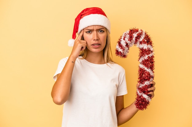 Giovane donna caucasica che tiene un grande bastone di natale isolato su sfondo giallo che mostra un gesto di delusione con l'indice.