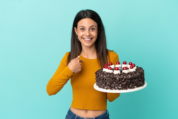 Young caucasian woman holding birthday cake isolated on blue background with surprise facial expression