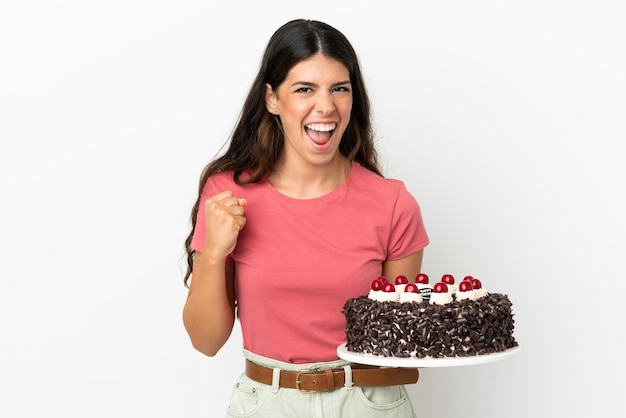 Young caucasian woman holding birthday cake isolated on white background celebrating a victory in winner position