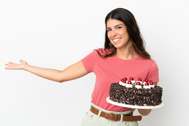 Young caucasian woman holding birthday cake isolated on white background extending hands to the side for inviting to come