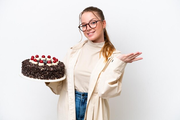 Young caucasian woman holding a Birthday cake isolated on white background extending hands to the side for inviting to come