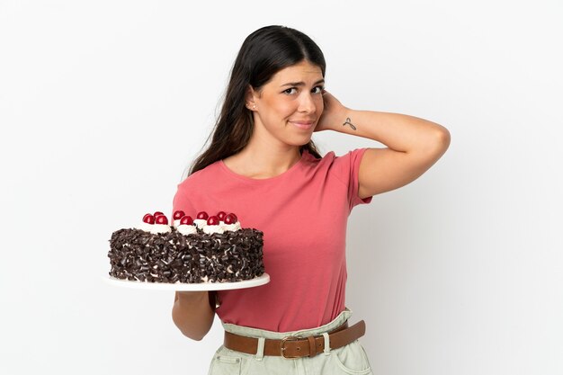 Giovane donna caucasica che tiene la torta di compleanno isolata su fondo bianco che ha dubbi