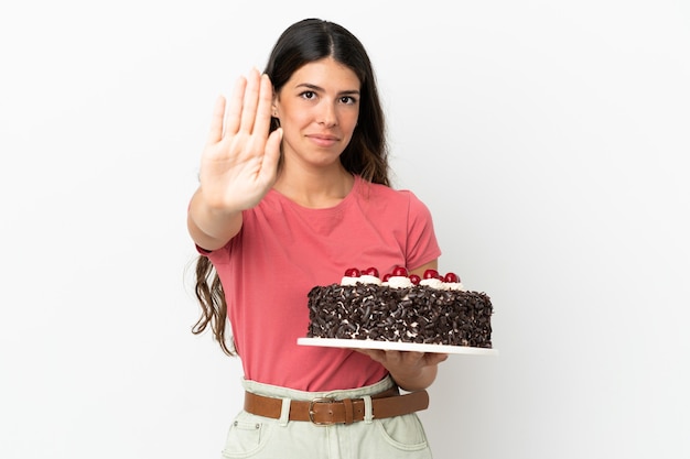 Young caucasian woman holding birthday cake isolated on white background making stop gesture