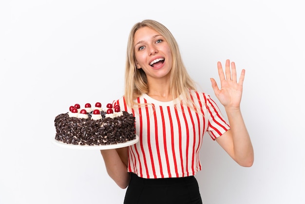 Young caucasian woman holding birthday cake isolated on white background saluting with hand with happy expression