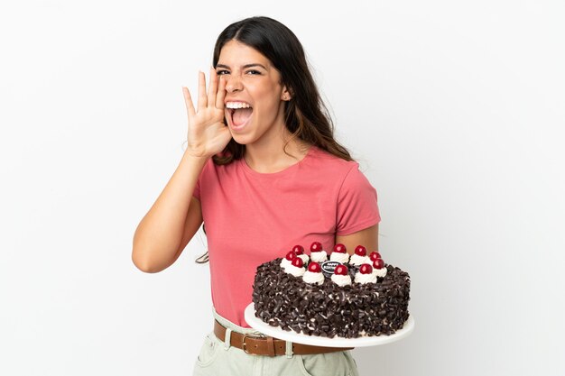 Young caucasian woman holding birthday cake isolated on white background shouting with mouth wide open