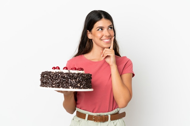 Young caucasian woman holding birthday cake isolated on white background thinking an idea while looking up