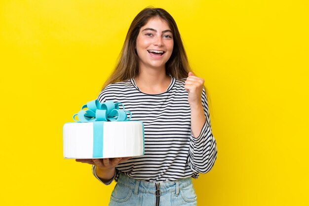 Young caucasian woman holding birthday cake isolated on yellow background celebrating a victory in winner position