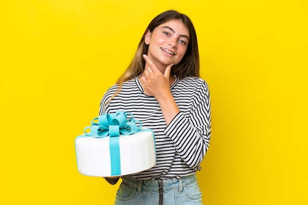 Young caucasian woman holding birthday cake isolated on yellow background happy and smiling