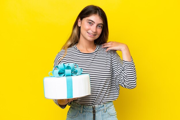 Young caucasian woman holding birthday cake isolated on yellow background laughing