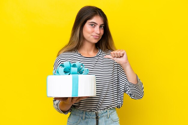 Young caucasian woman holding birthday cake isolated on yellow background proud and selfsatisfied