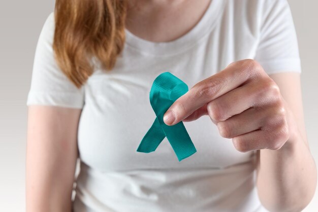 Young caucasian woman holding a bluegreen awareness ribbon for Stalking Awareness Month