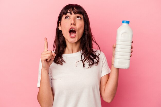 Young caucasian woman holding a bottle of milk isolated on pink background pointing upside with opened mouth.