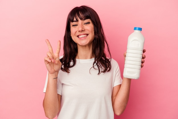 Young caucasian woman holding a bottle of milk isolated on pink wall showing number two with fingers