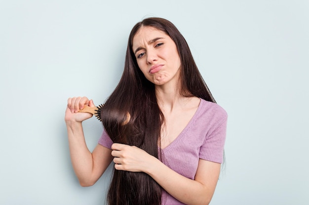 young caucasian woman holding a brush hair isolated on blue background
