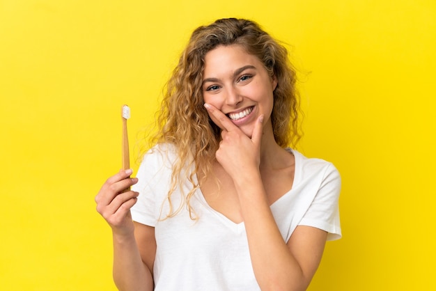 Young caucasian woman holding a brushing teeth isolated on yellow background happy and smiling