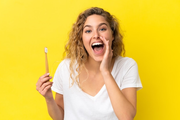 Giovane donna caucasica che tiene in mano un lavarsi i denti isolato su sfondo giallo che grida con la bocca spalancata