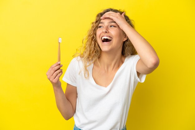 Giovane donna caucasica che tiene un lavarsi i denti isolato su sfondo giallo sorridendo molto