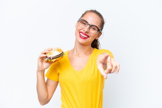 Young caucasian woman holding a burger isolated on white background pointing front with happy expression