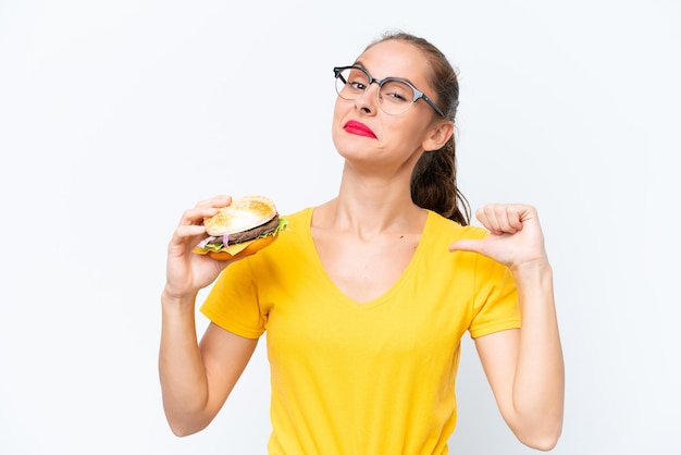 Young caucasian woman holding a burger isolated on white background proud and selfsatisfied