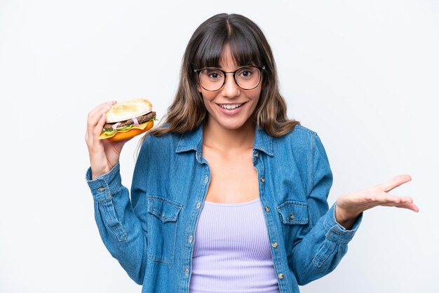 Foto giovane donna caucasica che tiene un hamburger isolato su sfondo bianco con espressione facciale scioccata