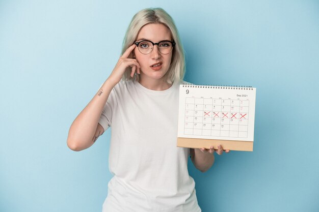 Giovane donna caucasica che tiene il calendario isolato su sfondo blu che mostra un gesto di delusione con l'indice.