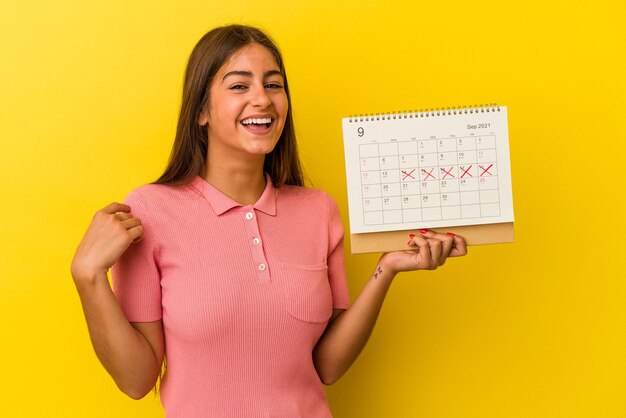 Молодая женщина кавказской, держащая календарь, изолированные на желтом фоне, смеясь и весело.