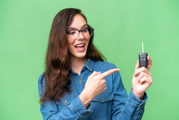 Young caucasian woman holding car keys over isolated background and pointing it