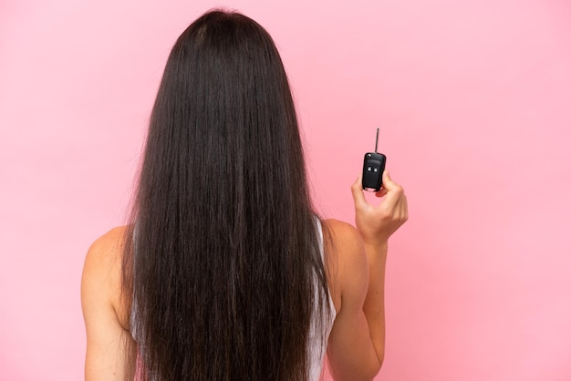 Young caucasian woman holding car keys isolated on pink background in back position