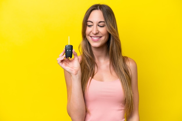 Young caucasian woman holding car keys isolated on yellow background with happy expression