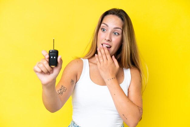 Young caucasian woman holding car keys isolated on yellow background with surprise and shocked facial expression