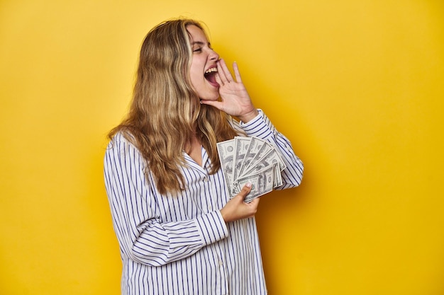 Photo young caucasian woman holding cash shouting and holding palm near opened mouth