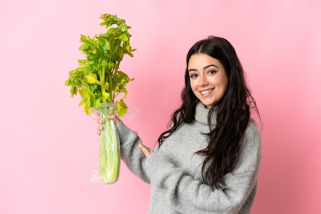 Young caucasian woman holding a celery isolated on blue background and pointing it